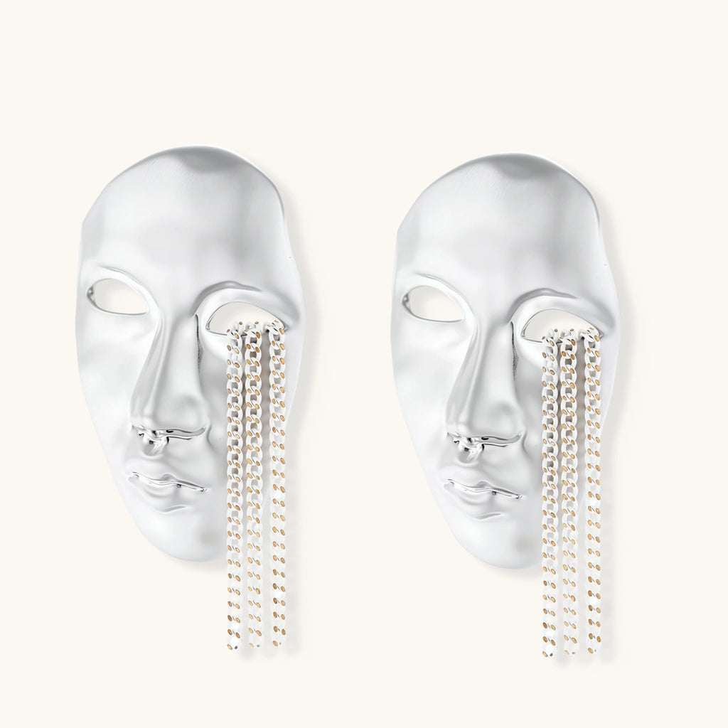Silver face-shaped statement earrings with flowing chain tassels hanging from sculpted lips on cream background